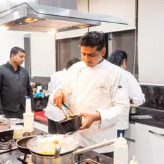 A chef carefully transfers a freshly cooked item from a pan, focused on the task at hand. This level of concentration is key to our quality.
