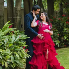 A tender moment captured during an outdoor maternity shoot. The vibrant red gown adds a touch of glamour, while the focus remains on the couple's loving connection.