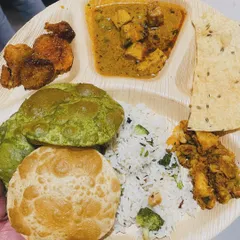 A look at our complete homestyle thali. This one features fluffy pooris, including a vibrant palak poori, served with paneer curry, vegetable rice, a dry vegetable side, papad, and fried potatoes.