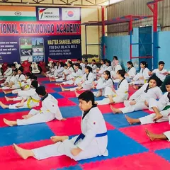 Discipline starts with the basics. A class of students in doboks of various belt colors performs synchronized stretching exercises on the safety mats of our dojang.