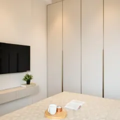A different angle of the same room, showing the minimalist aesthetic. The floor-to-ceiling wardrobe doors in a neutral beige laminate and a floating console under the TV keep the space feeling light and airy.