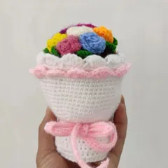 A miniature crochet bouquet featuring a rainbow of small flowers, held in a white crocheted wrap with a pink ribbon. These are perfect as a small, thoughtful gift.