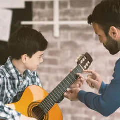 We provide hands-on guidance in our one-on-one instrumental classes. Here, an instructor helps a young student with correct finger placement for chords on an acoustic guitar, an essential step in mastering the instrument.