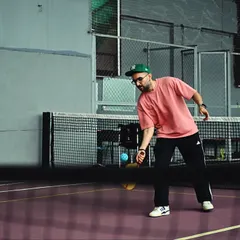 A player lunges for a low shot at the net during a pickleball game. The purple court and indoor setting ensure a perfect game, day or night.