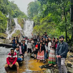 A large group enjoying the refreshing spray of a waterfall during an Independence Day trip. These waterfall visits are a perfect way to cool down and have fun.