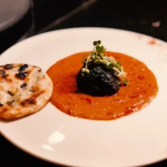 A modern Indian creation, where a spiced kofta rests in a pool of rich, flavourful gravy, served alongside a delicate naan. The artistic plating with microgreens elevates a classic concept into a gourmet experience.