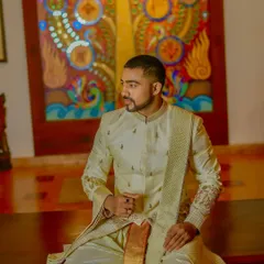 This seated pose highlights the beautiful drape of the silk dhoti and the intricate embroidery on the sleeve of the sherwani. Every element is designed for both aesthetic appeal and comfort.