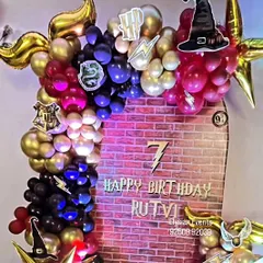 A detailed Harry Potter-themed backdrop for Rutvi's 7th birthday. The design includes a brick wall print, house logos, a sorting hat cutout, and a balloon garland in house colors, creating a magical photo corner.