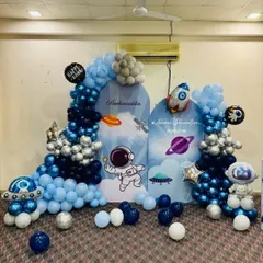 An out-of-this-world space theme party with custom astronaut and planet backdrops. The scene is framed by a galaxy-inspired balloon arrangement in shades of blue, silver, and navy.