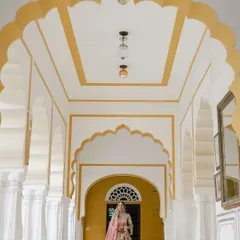 The bride stands in a majestic palace corridor, framed by ornate yellow and white arches. This shot uses the architectural symmetry to create a powerful and graceful bridal portrait.