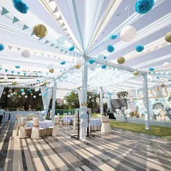 An expansive outdoor tented area for a royal celebration, with flowing white and blue drapes creating a dreamy canopy. The space is elegantly set with coordinated tables and chairs, ready to host guests in style.