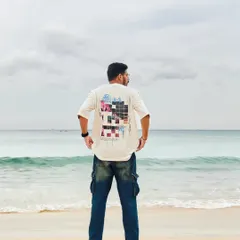 A back-facing shot on a beach in Thailand, showcasing a cool graphic tee against the backdrop of the ocean. It's about capturing the vibe of a place through fashion and mood.