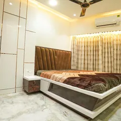 This master bedroom design balances modern and classic elements. It features a custom bed with an upholstered headboard and a high-gloss white wardrobe with subtle gold inlay details.