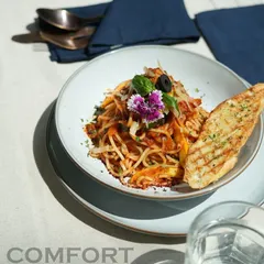 My take on a comfort classic. This is my tangy arrabbiata spaghetti, tossed with fresh vegetables, garnished with an edible flower, and served with a slice of perfectly grilled garlic bread. It’s a simple dish, elevated.