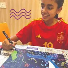 Adding details with a paint marker is a great way to create crisp lines and patterns over a painted background. Here, a student adds coral details to her ocean scene.