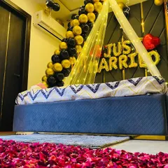 This low-angle shot shows the full romantic effect, with a pathway of red rose petals leading to the decorated bed. The combination of black and gold balloons with the 'Just Married' sign creates a luxurious feel.