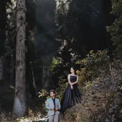 A fairytale-like shot in a dense forest, with sunbeams breaking through the trees. The couple's formal attire contrasts beautifully with the wild, natural setting.