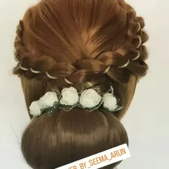 This classic bun is elevated with a crown of braids, interwoven with a fine gold thread. A line of small white flowers at the base adds a soft, traditional touch, making it suitable for both muhurtham and party looks.