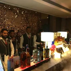 Our smiling team of bartenders and butlers, ready to serve at a glamorous event with a sequin backdrop.