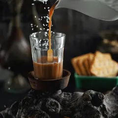 An artistic shot of "cutting chai" being poured, with sugar crystals appearing to fall alongside the stream of tea. This creative, moody photograph elevates a simple daily ritual into a moment of visual poetry.