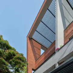 This apartment facade features a combination of exposed brick and a slatted pergola roof. These elements frame the sky and create dynamic shadows, adding texture and depth to the building's exterior.