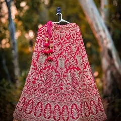 A stunning shot of the bride's red wedding lehenga, detailed with intricate gold embroidery, hanging in a natural setting.