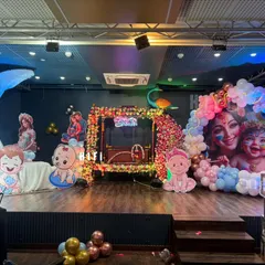 A grand stage setup for a baby shower or naming ceremony. This decor features a large moon prop, a decorated cradle, and multiple character cutouts with a Krishna theme.