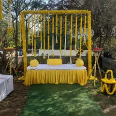 A classic Haldi ceremony setup, radiating pure joy and tradition. The backdrop is crafted entirely from bright yellow marigold garlands, creating a perfect, sun-kissed space for this happy occasion.