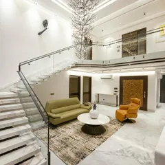 A breathtaking double-height living area where a massive, tree-like crystal chandelier cascades down, acting as a sculptural centerpiece. The space is defined by its grand scale, marble flooring, and a floating staircase with glass railings.