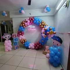 A circular balloon ring is a stylish alternative to a traditional arch for a baby shower or gender reveal. This design uses a mix of pink, blue, and gold balloons, B-A-B-Y blocks, and character cutouts, all centered around a glowing "Baby Shower" neon sign.
