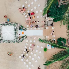 An aerial drone shot of a beach wedding ceremony in Thailand. This perspective shows the beautiful layout of the event, with the guests seated on the sand and the elegant mandap positioned right by the water's edge.