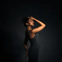 A full-body shot using negative space to create a sense of isolation and drama. The single light source highlights the model's form against the dark background.