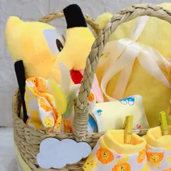 This detailed view inside the newborn welcome basket shows the soft yellow blanket, a Pluto plush toy, and a set of comfortable baby clothes, all packed and ready for gifting.