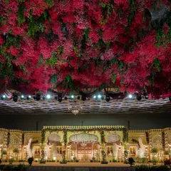 I transform grand ballrooms into royal courts. This wedding stage is defined by its magnificent ceiling, a dense canopy of crimson and green florals that creates an atmosphere of immersive, regal opulence and provides a breathtaking backdrop for the ceremony.