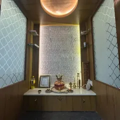 The interior of the pooja unit, showcasing the intricate "Vishnu Sahasranamam" carving on the back panel. The glass shelves and warm lighting create a divine and serene ambiance.