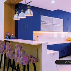 A vibrant blue kitchen designed for someone who loves color. The bold cabinetry is balanced by a white marble countertop and backsplash. The integrated breakfast bar with patterned stools creates a perfect spot for casual meals.