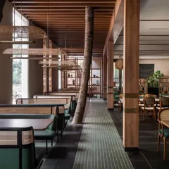 A full view of the main dining hall where we integrated existing tree trunks directly into the restaurant's layout. The custom booth seating and suspended light fixtures were designed to complement the natural elements, creating a unique indoor-outdoor restaurant interior.