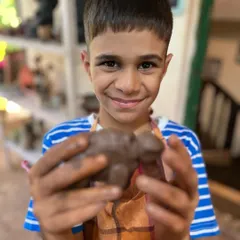 The proud smile of a young artist holding his finished clay turtle. Our workshops for kids are designed to be fun, engaging, and a great way to boost creativity.