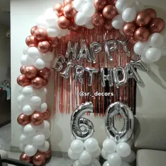 A classic and elegant 60th birthday decoration with a rose gold curtain backdrop, 'Happy Birthday' foil letters, and a white and rose gold balloon arch.