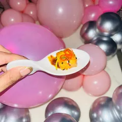 A single, flavourful bite of a salmon appetizer, held up against the party's pink and silver balloon decor.