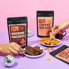 A fun, party-themed shot of Atom Eats Brownie and Coffee Nachos. The hands reaching in to snack and the disco balls create a celebratory vibe perfect for social media.