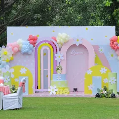 An enchanting outdoor setup for a "Sunshine & Pastel Rainbows" first birthday. This backdrop features whimsical pastel arches, giant balloon daisies, and a custom cake stand, all designed to create a bright and joyful atmosphere in a garden setting.