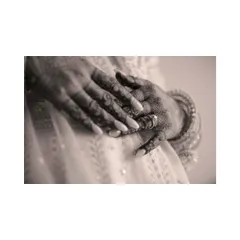 A black and white close-up of the bride's hands, focusing on her engagement ring and the delicate mehendi.