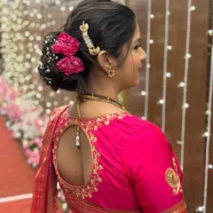 A classic and elegant bridal bun for a Maharashtrian wedding. The hairstyle is adorned with beautiful pink flowers and a traditional hair accessory, perfectly complementing the silk saree.