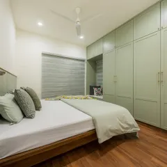 A full view of a minimalist bedroom, where sage green wardrobes with a built-in window seat provide ample storage and a cozy nook. The wooden floor and bed frame add natural warmth to the space.