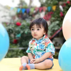 A toddler sits peacefully in an outdoor setting, surrounded by balloons. This portrait captures a quiet, contemplative moment, showcasing the child's natural curiosity.