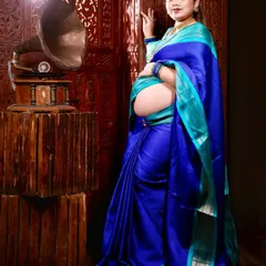 A full-length portrait incorporating a vintage gramophone. This prop adds a touch of nostalgia and artistry to the traditional saree maternity shoot.