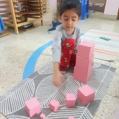 The iconic Pink Tower is a classic Montessori sensorial material. As this child carefully stacks the blocks from largest to smallest, they are visually discriminating dimensions, refining their motor control, and developing a mathematical mind.