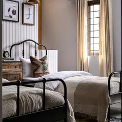 A closer look at one of the twin beds in the boys' room. The black iron bed frame, patterned pillow, and warm lighting from the leather sconce create a cozy and personalized sleeping nook.