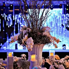 The tablescape for a modern Sangeet, featuring a dramatic centerpiece of dried branches and white orchids against a backdrop of a cascading blue light installation.